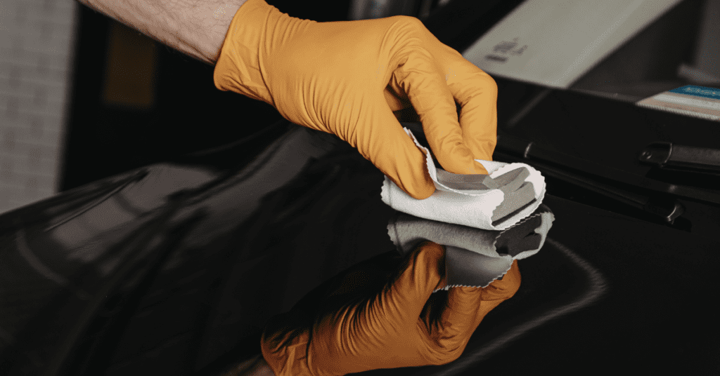 Gloved hand polishing a glossy black car surface with a cloth