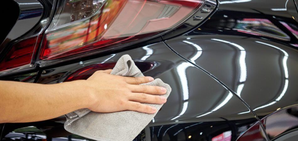 Hands polishing a black car with a microfiber cloth under bright lights