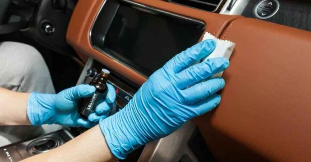 Blue-gloved hands cleaning a car dashboard with a cloth and spray bottle