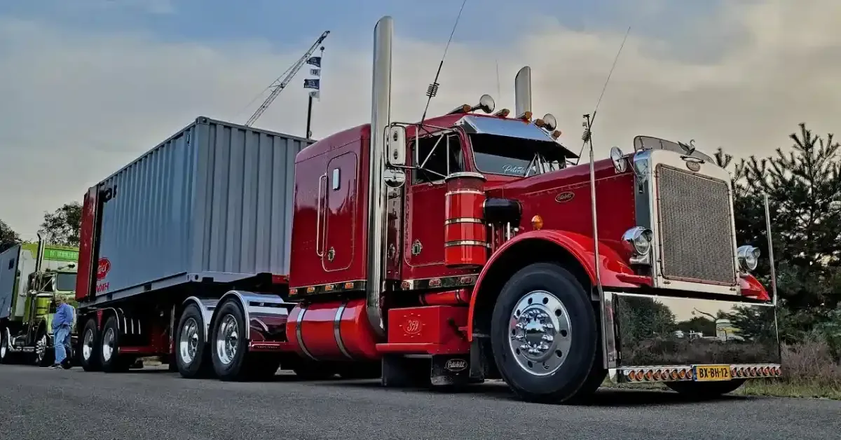 Red semi truck hauling a gray shipping container on a highway under a cloudy sky