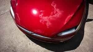 Front view of a shiny red car on pavement, with the front bumper visible.