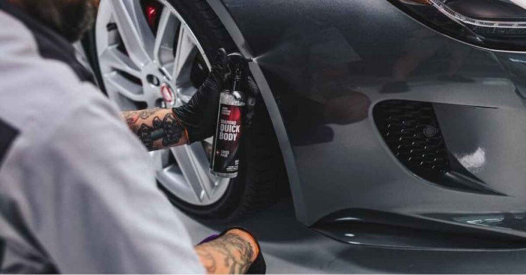 Person spray-painting a silver sports car’s front wheel and side panel in a garage