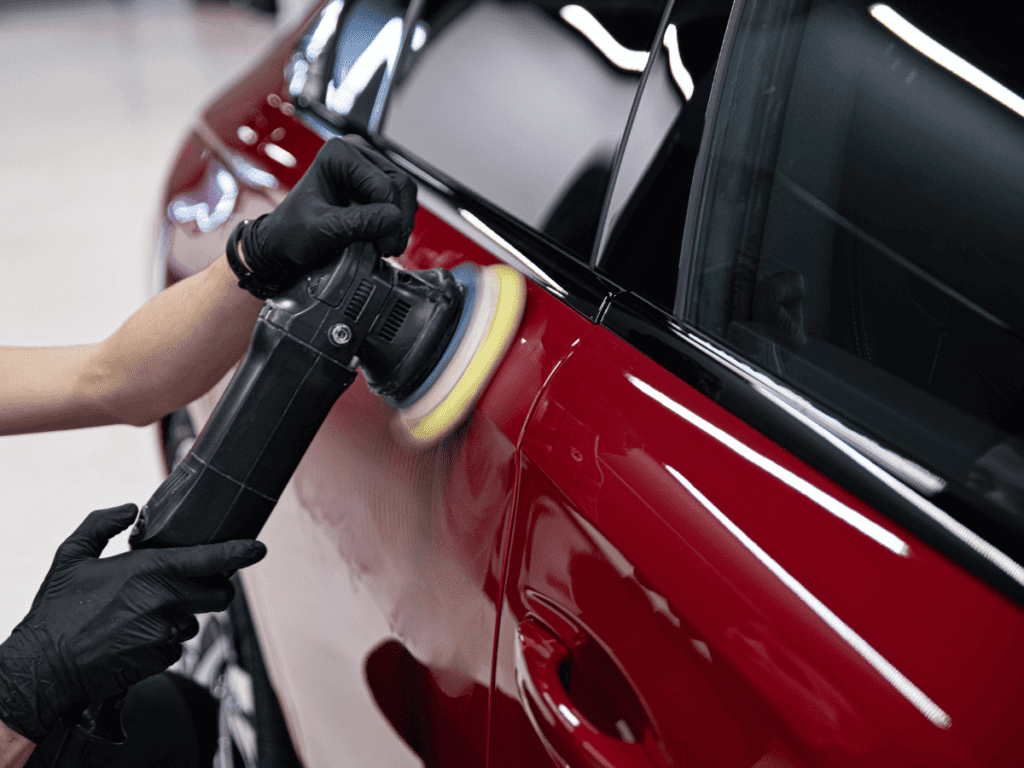 Gloved hands polishing a red car with a buffer near the rear window