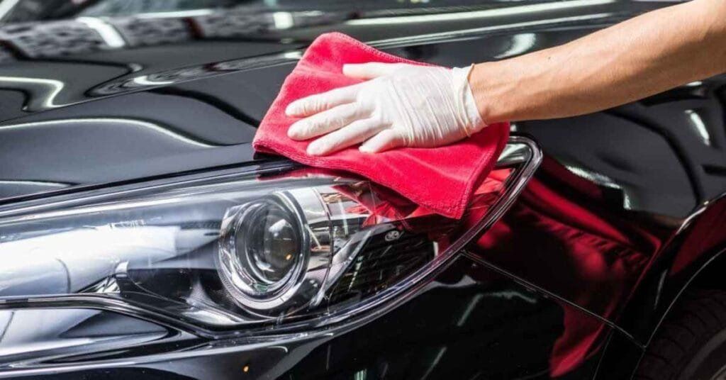 Person wiping a black car headlight with a red cloth during detailing