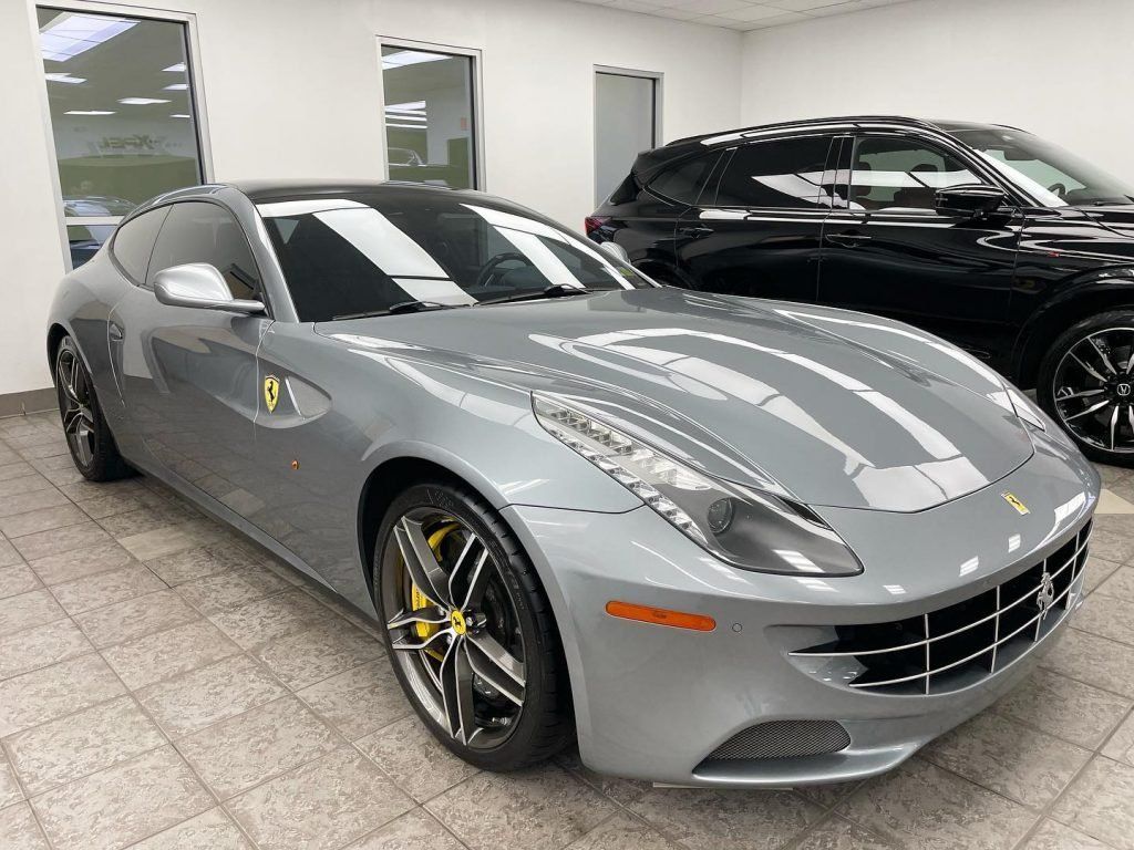 Silver Ferrari sports coupe in a showroom, with a black SUV parked behind it.