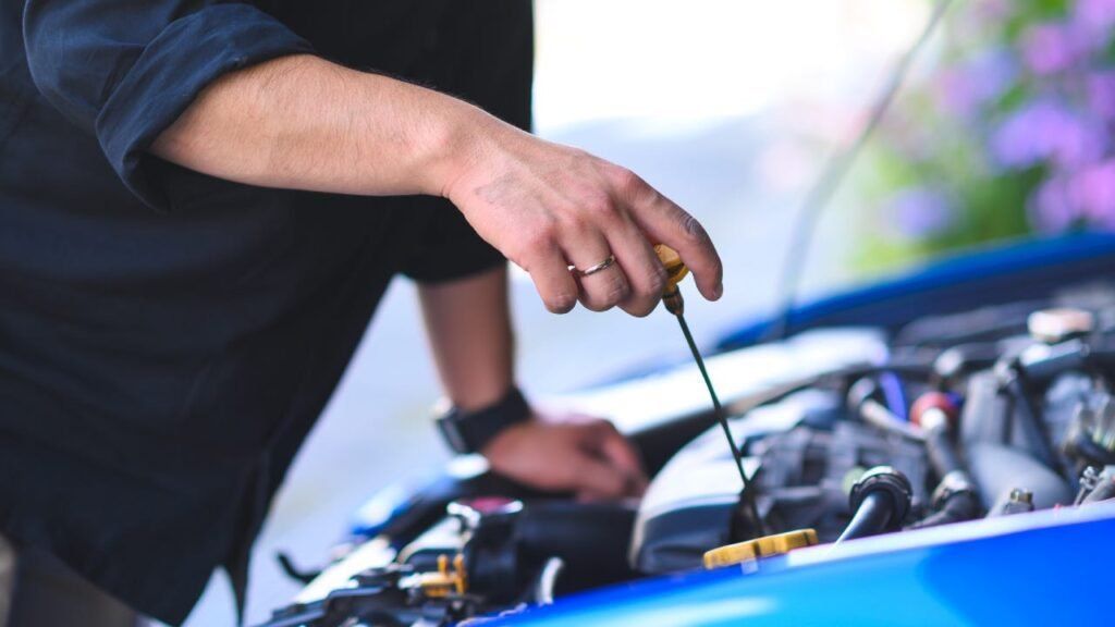 Person checking engine oil with dipstick under open car hood