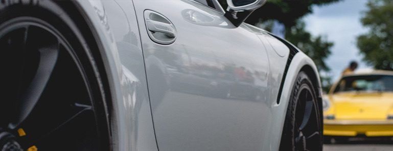 Close-up of a silver sports car beside a yellow car on a road
