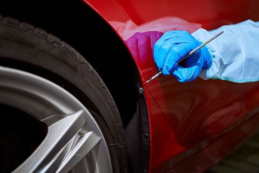 Gloved hand using a detailing tool on a red car near the rear wheel
