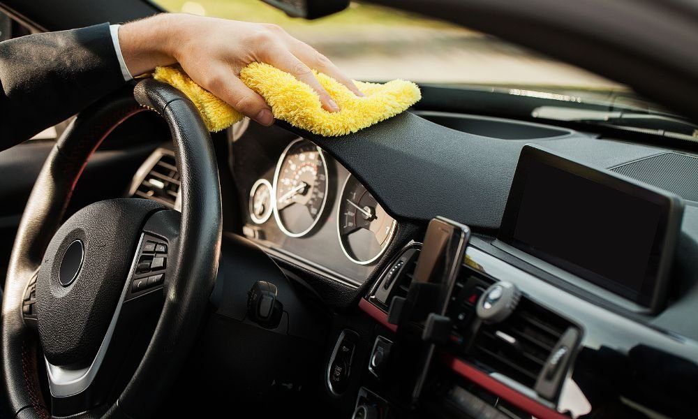 Hand wiping dust from a car dashboard with a yellow cloth