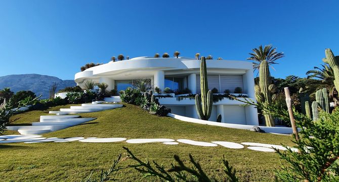 Modern white hillside villa with palm trees and a green lawn under a clear blue sky