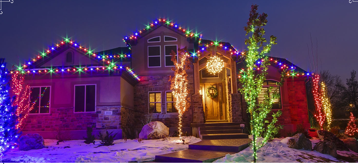 A house decorated for Christmas with colorful lights on the roof and trees. Snow covers the ground.