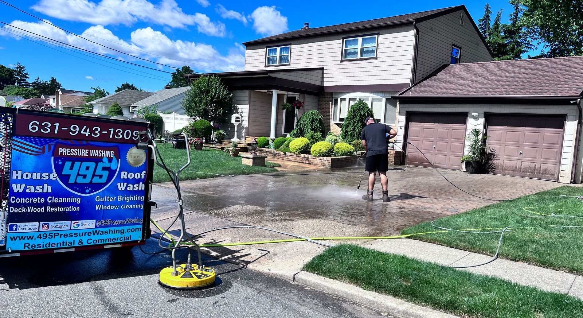 A person power washing a driveway in front of a two-story house. A sign for 