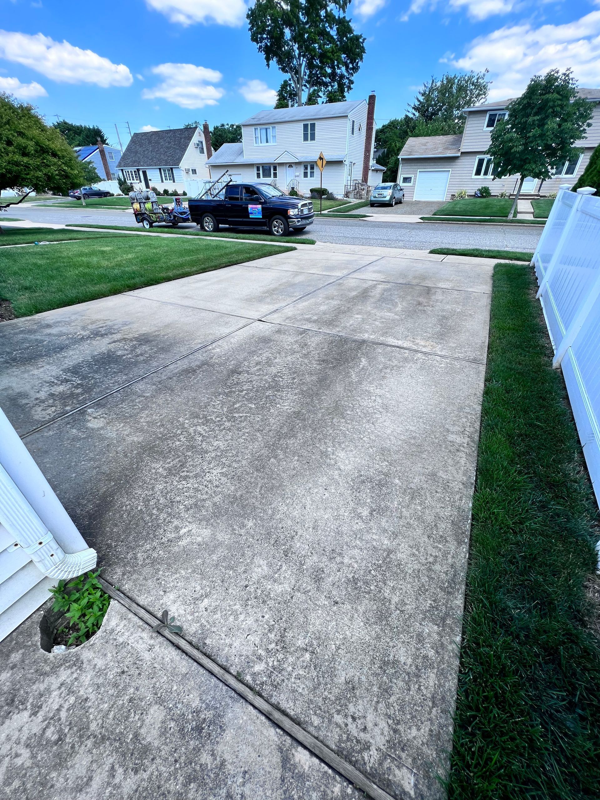 Driveway with a truck pulling a trailer in a residential neighborhood on a sunny day. Green grass borders the driveway.