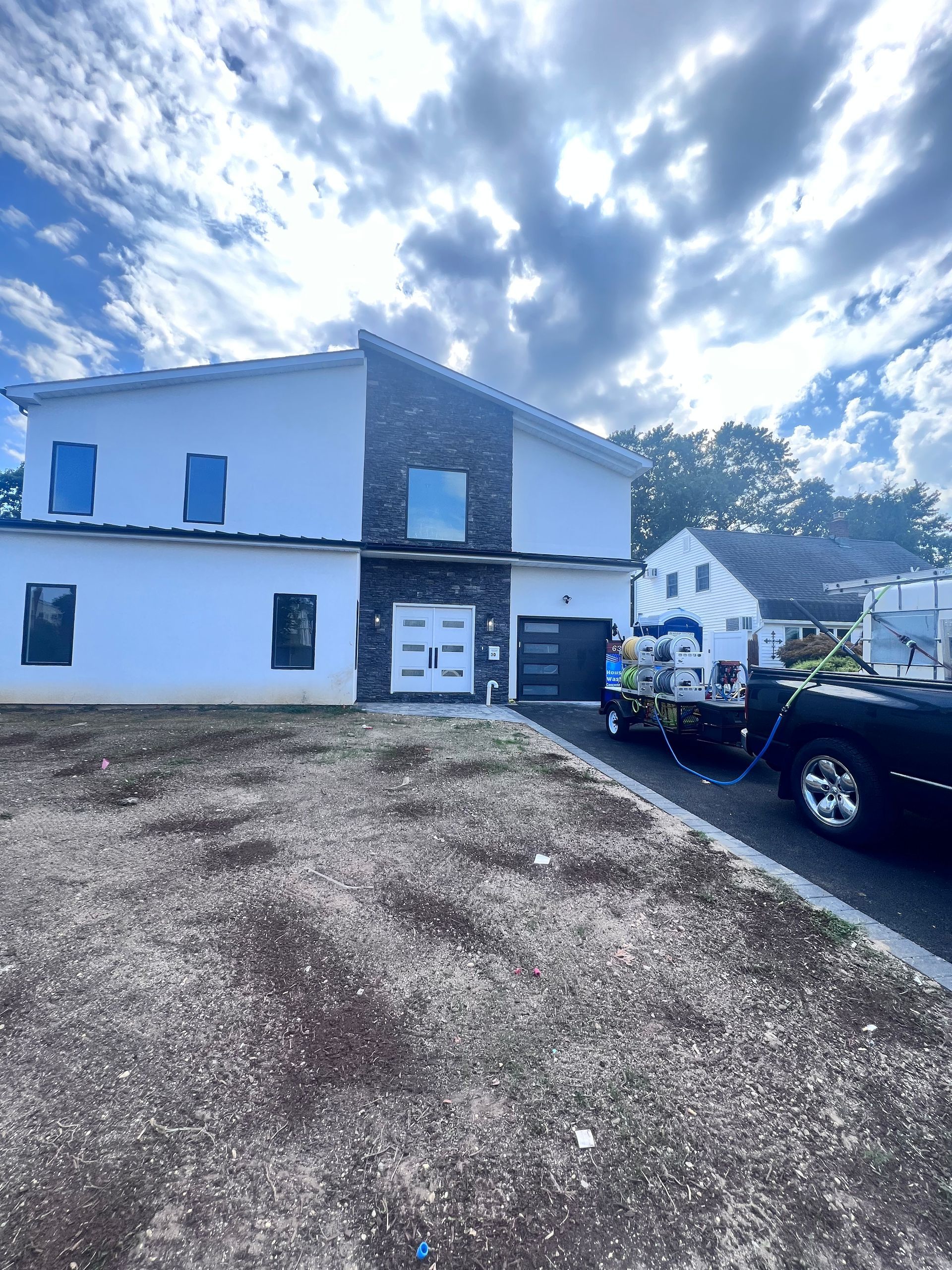 Two-story modern house with white stucco and a dark brick accent, on a cloudy day. A black car is in the driveway.