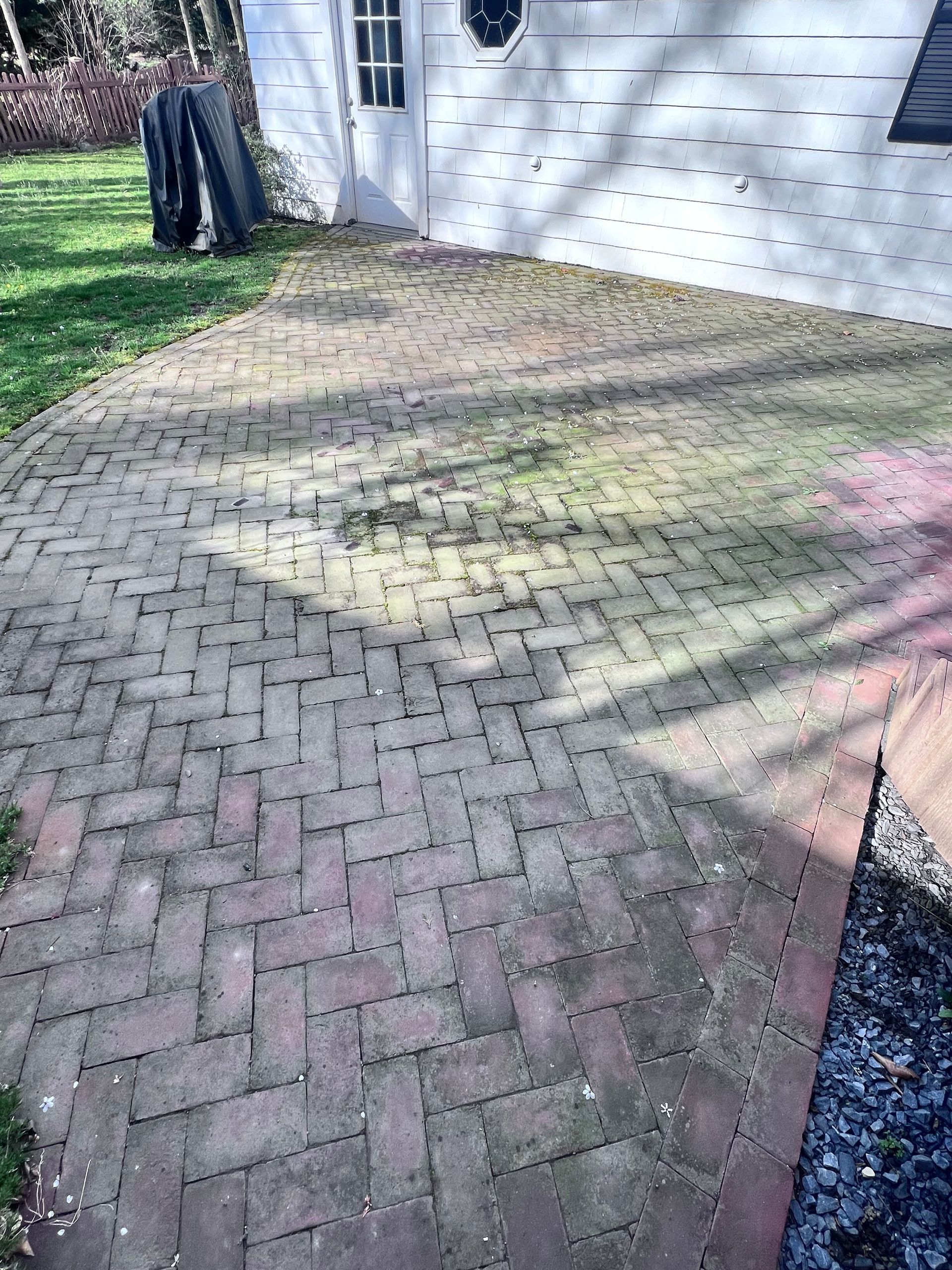 Brick patio with herringbone pattern next to a white building. The bricks are weathered with moss and sunlight.