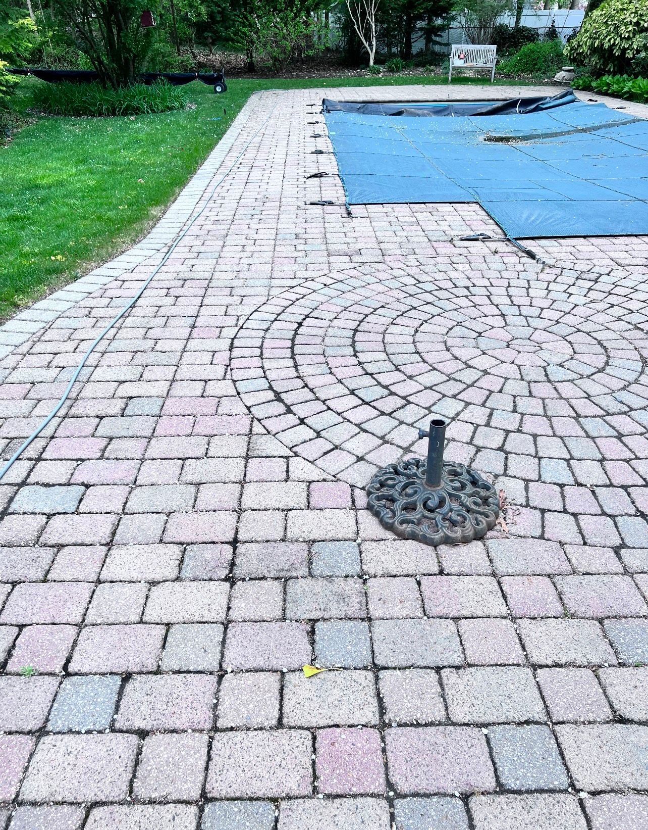 Brick patio surrounding a pool, featuring a circular design. A metal umbrella stand is visible on the patio.