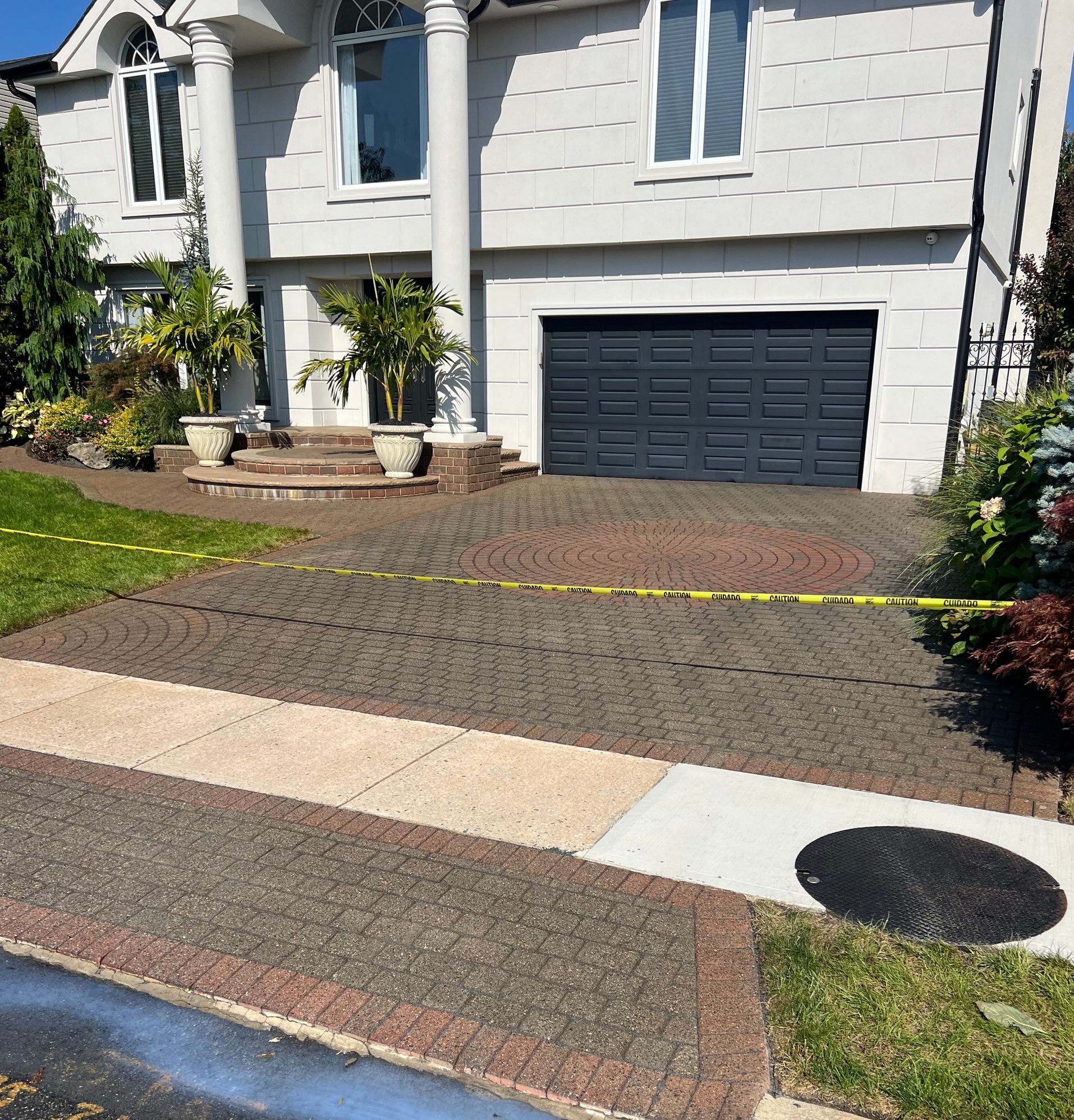 A house with a brick driveway; yellow tape blocks the way. The garage door is dark grey.