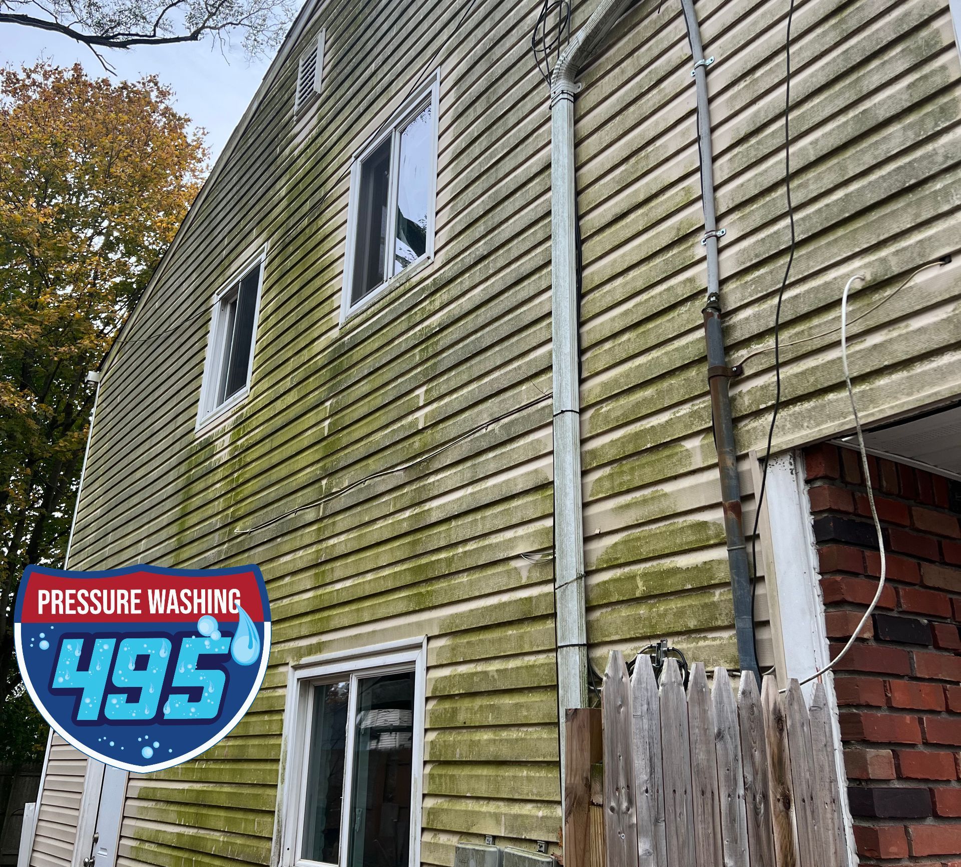 A two-story house with green algae on the siding. The pressure washing company logo is in the bottom left.