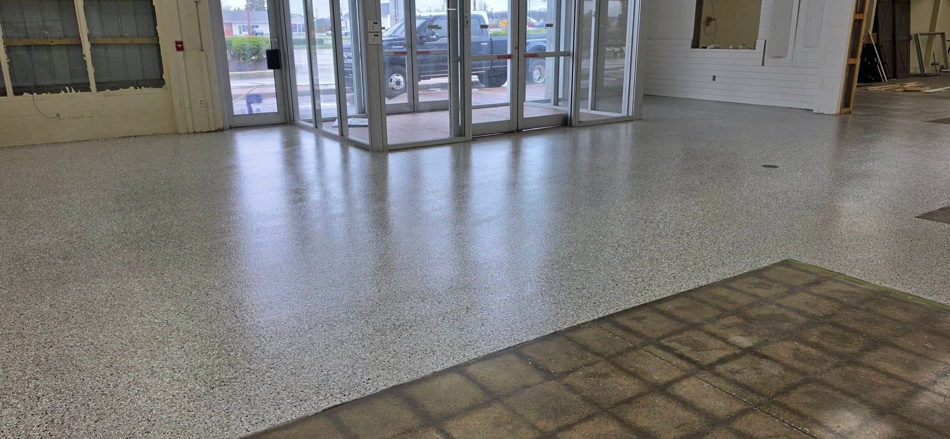 Empty lobby with terrazzo floor, glass entrance doors, and tiled walkway in the foreground