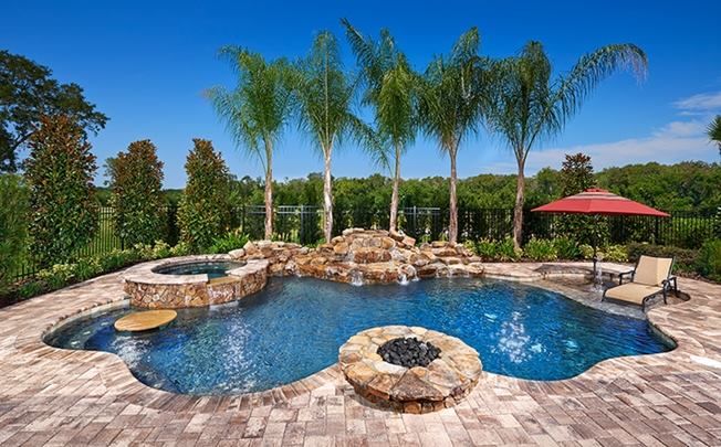Luxurious backyard pool with a waterfall, hot tub, and fire pit under a clear blue sky.