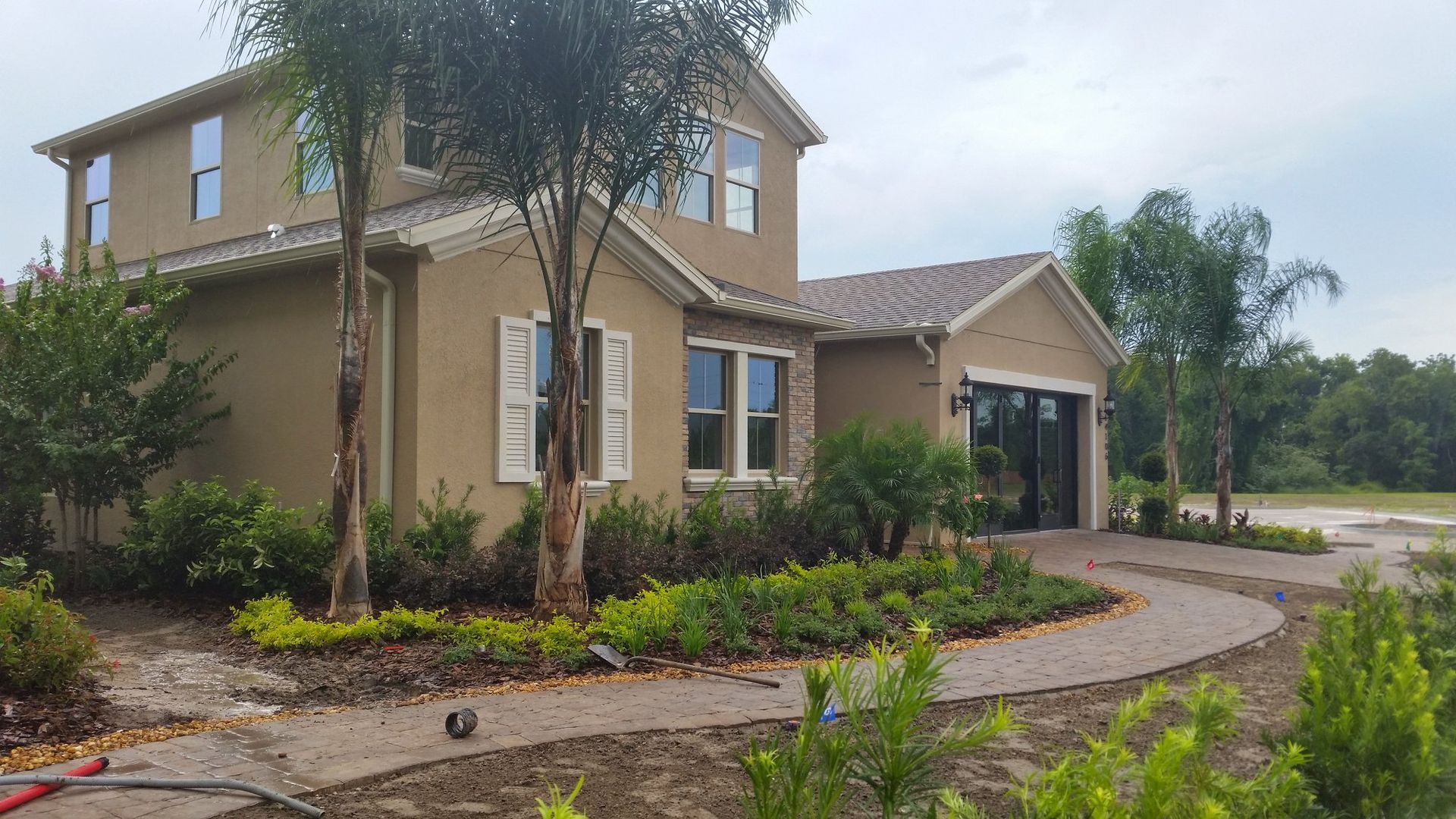 Two-story tan house with landscaping and a curved walkway leading to the front door; overcast day.
