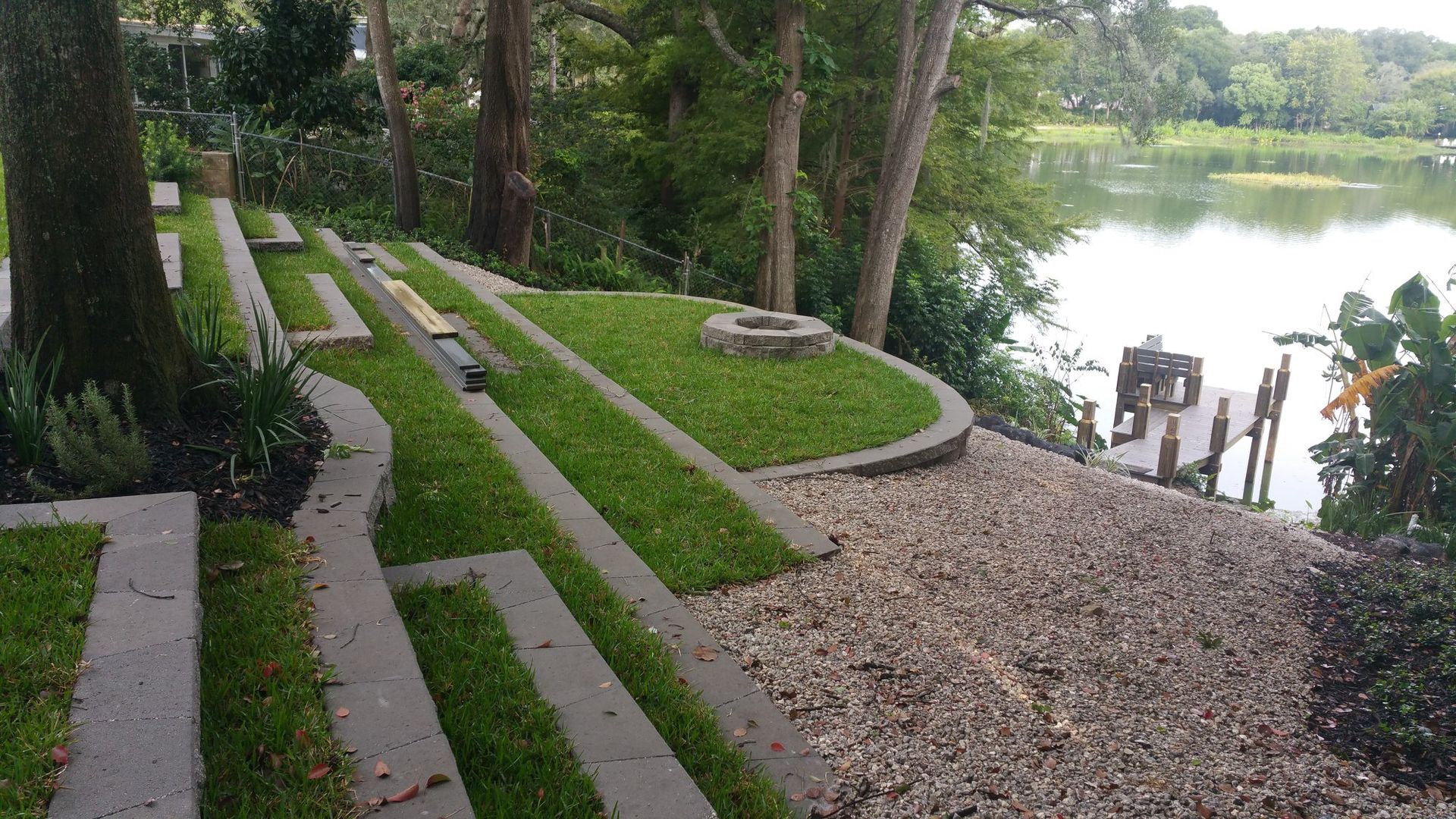 Landscape with terraced concrete, grass, gravel, and a lake.