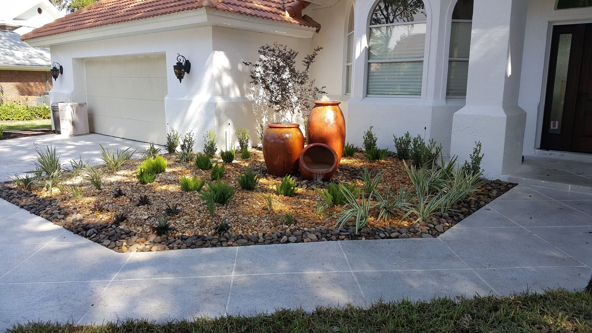 Front yard landscaping with decorative pots, plants, and a concrete walkway. White house with a terracotta tile roof.