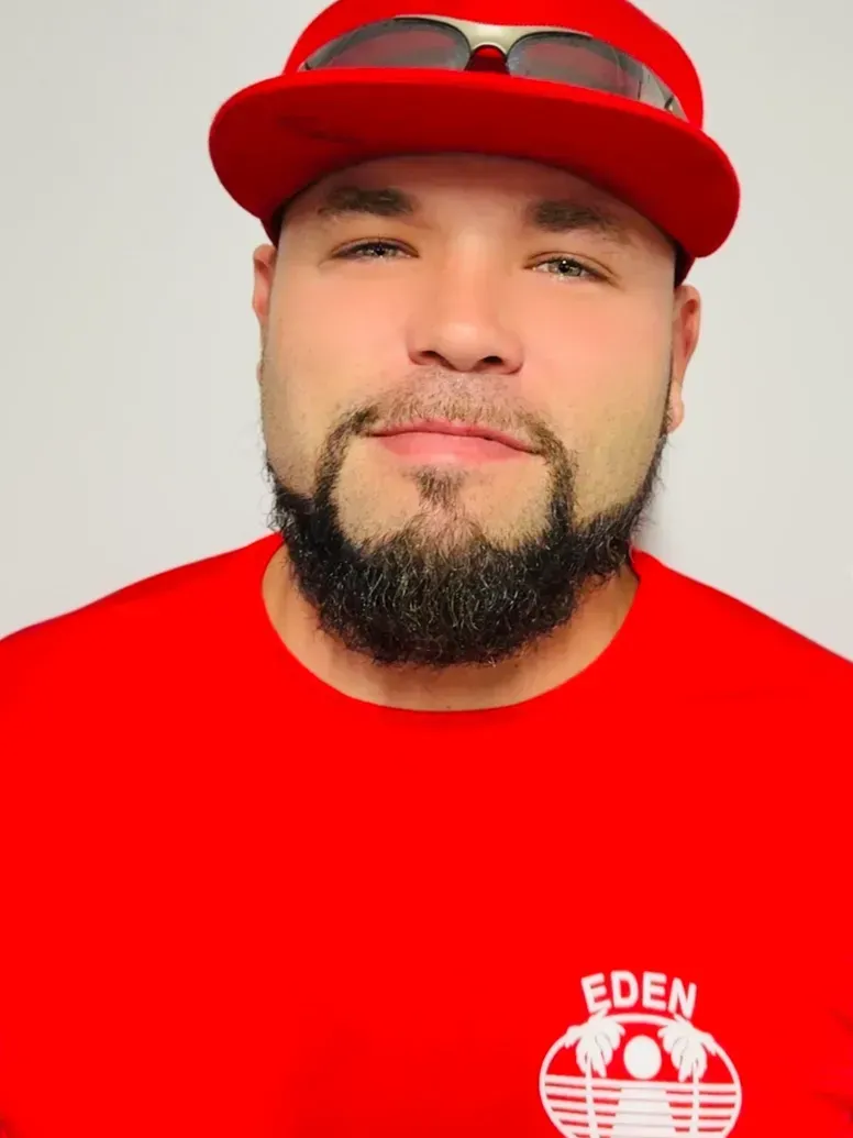 Man wearing red cap and shirt with a logo, sunglasses, and goatee, smiling.