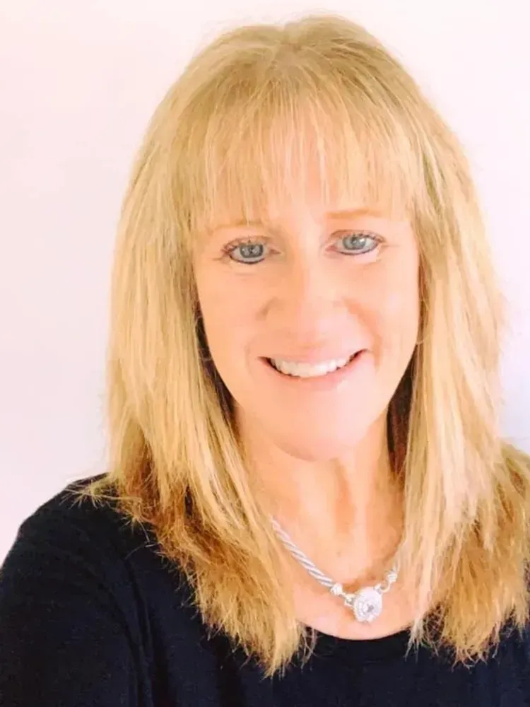 Woman with blonde hair smiling, wearing a black shirt and necklace.