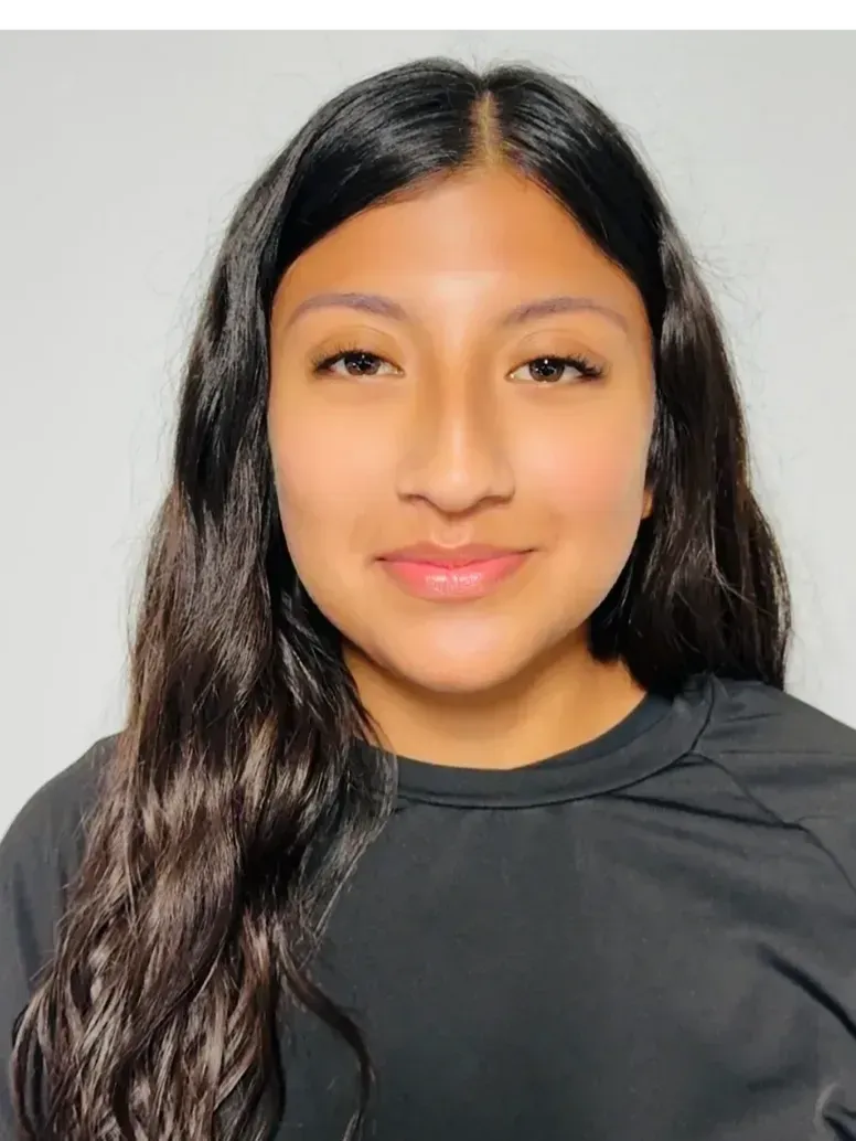 Woman with dark hair smiles, wearing a black shirt, against a light gray background.