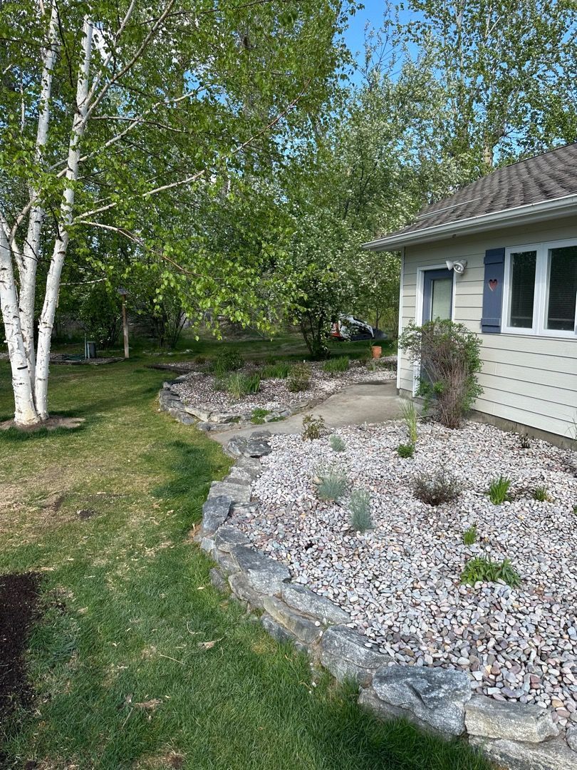 Green lawn and rock garden border a house with white siding and blue shutters.