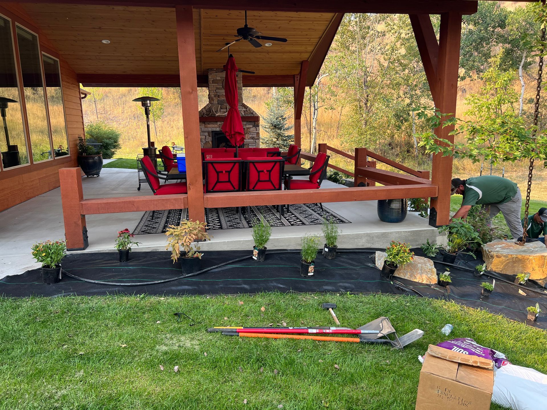 A person planting flowers near a porch with outdoor furniture; green grass in the foreground.