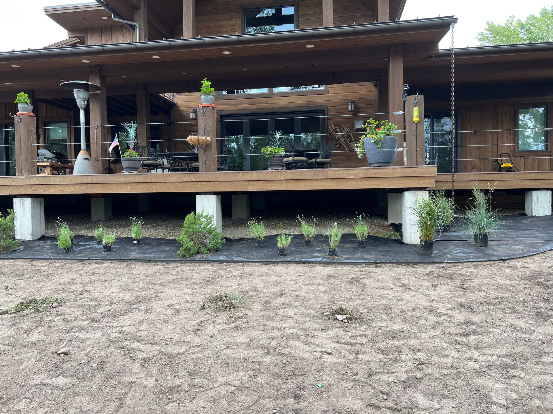 A wooden deck extends from a house, with plantings in front on black fabric.