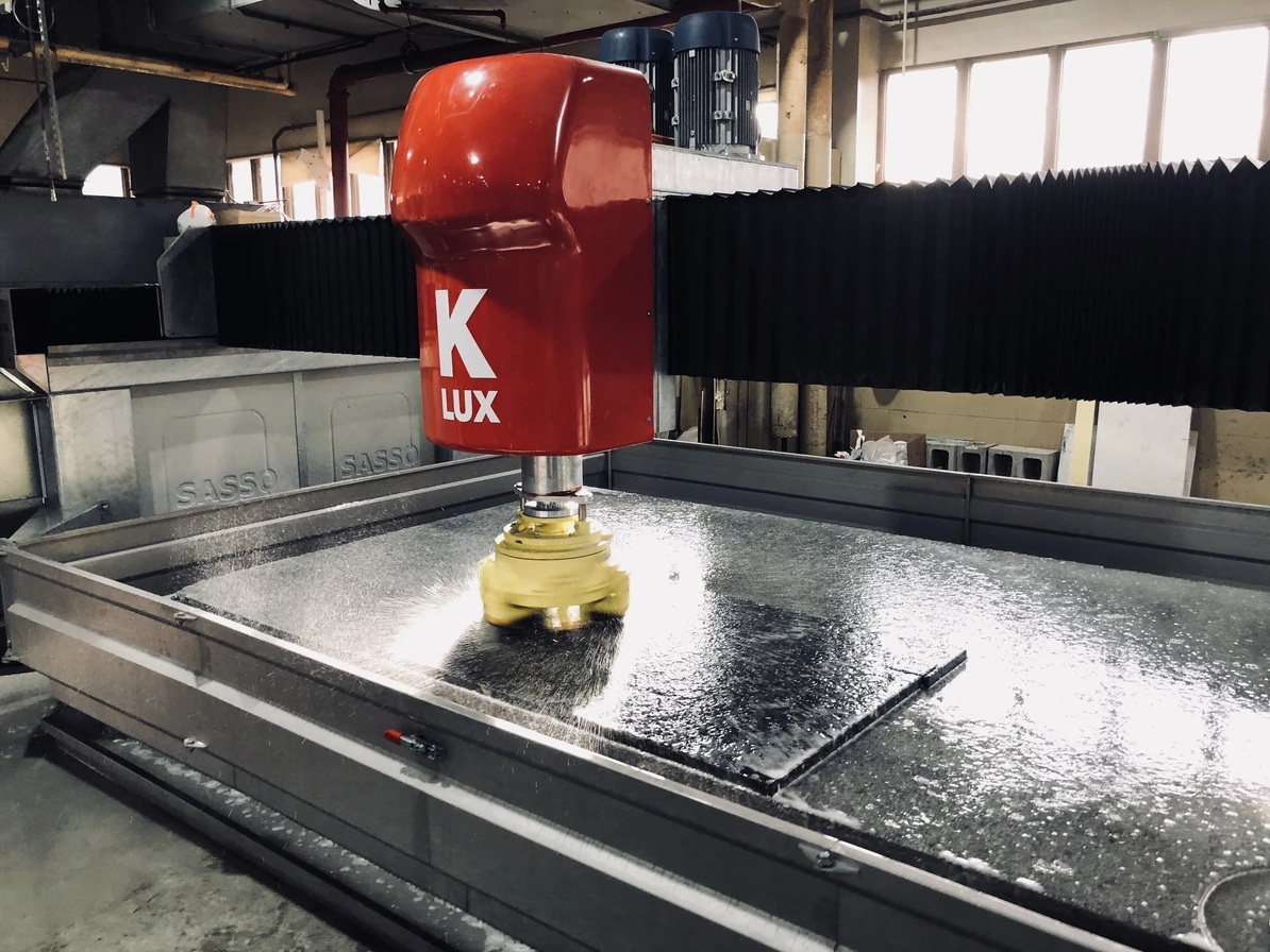 A red LUX machine grinding a sheet of dark material with water in a factory.