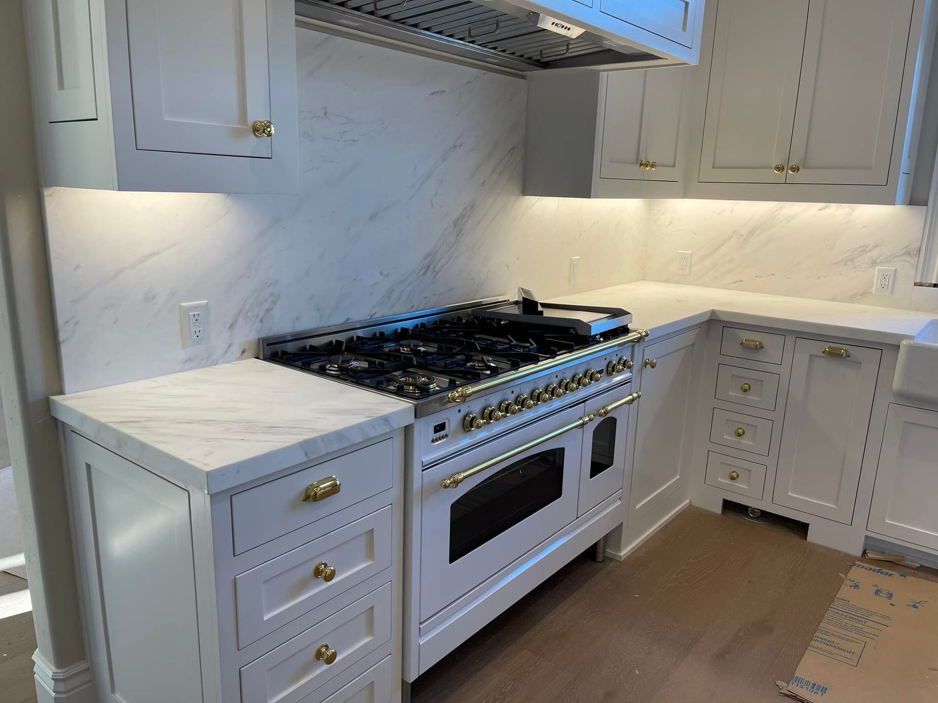 White kitchen with marble backsplash, gas range, and cabinets with gold hardware.