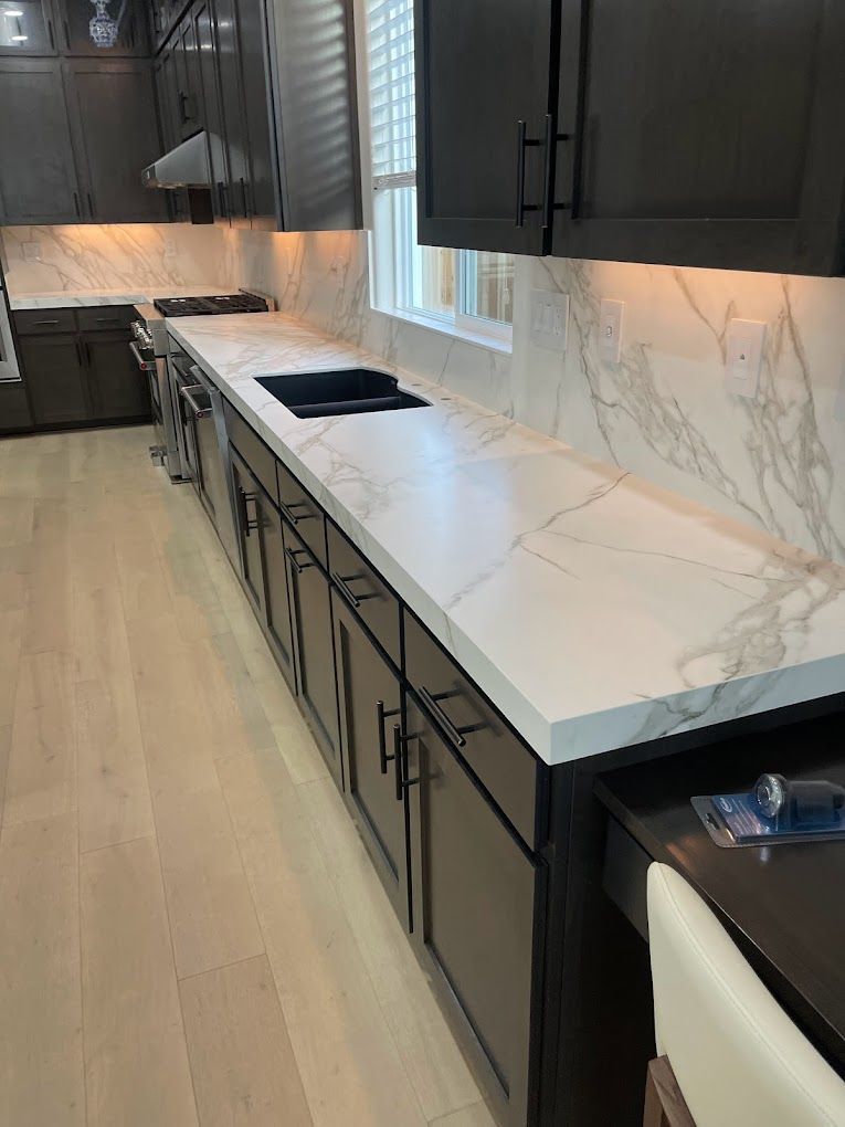 A kitchen with marble counter tops and black cabinets.