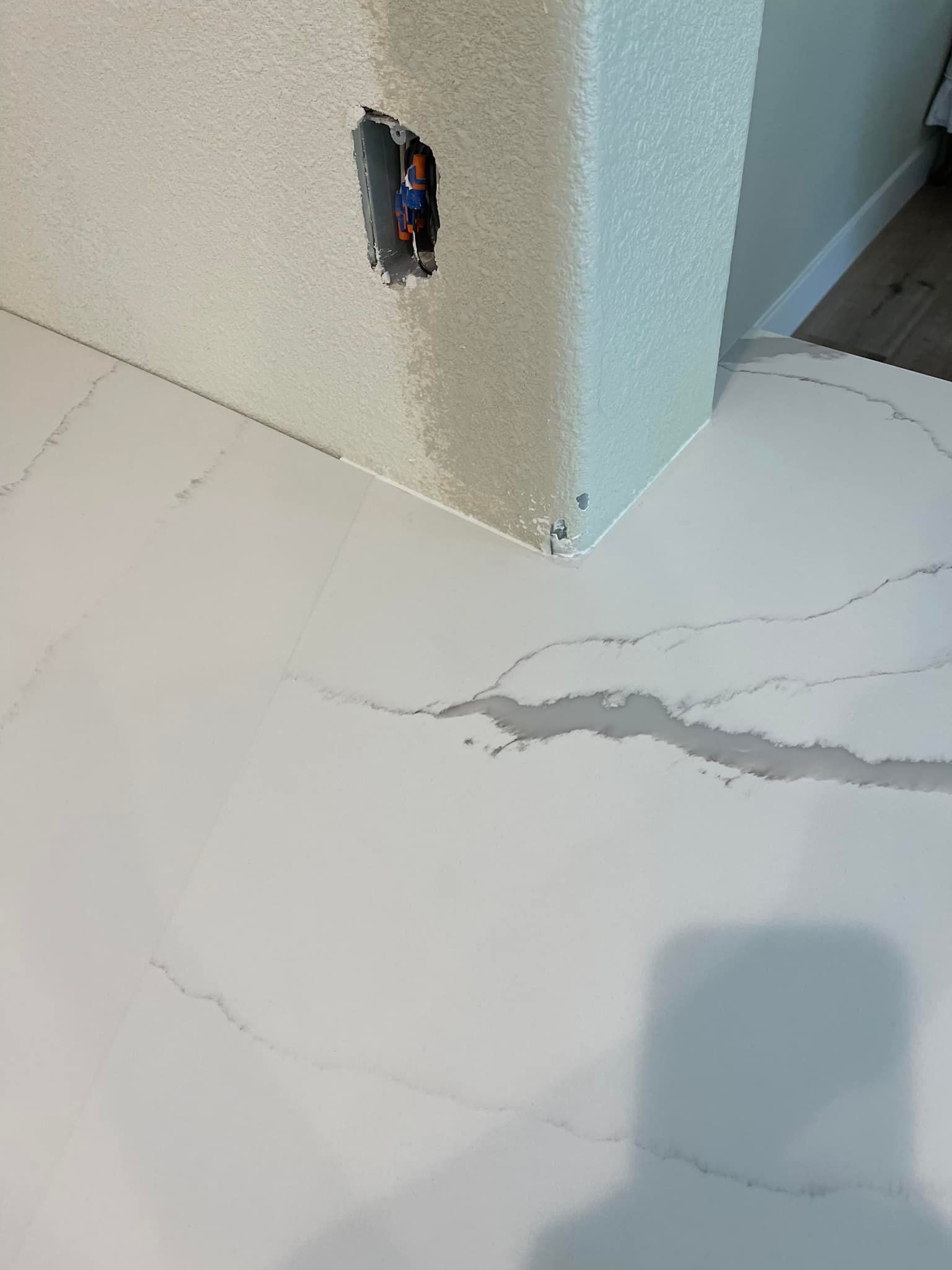 White countertop with gray veining meeting a textured, light-colored wall with an electrical outlet.