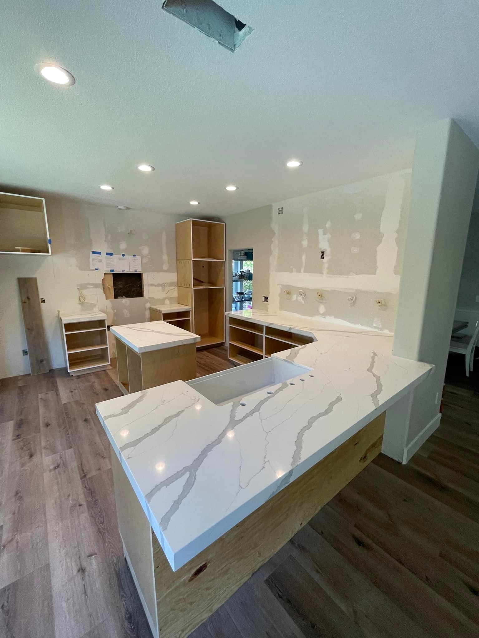 Kitchen under renovation with white countertops, wood cabinets, and drywall.