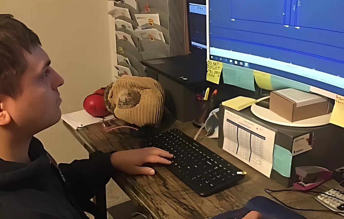 A person at a computer editing video, side profile, looking at the monitor, cluttered desk.