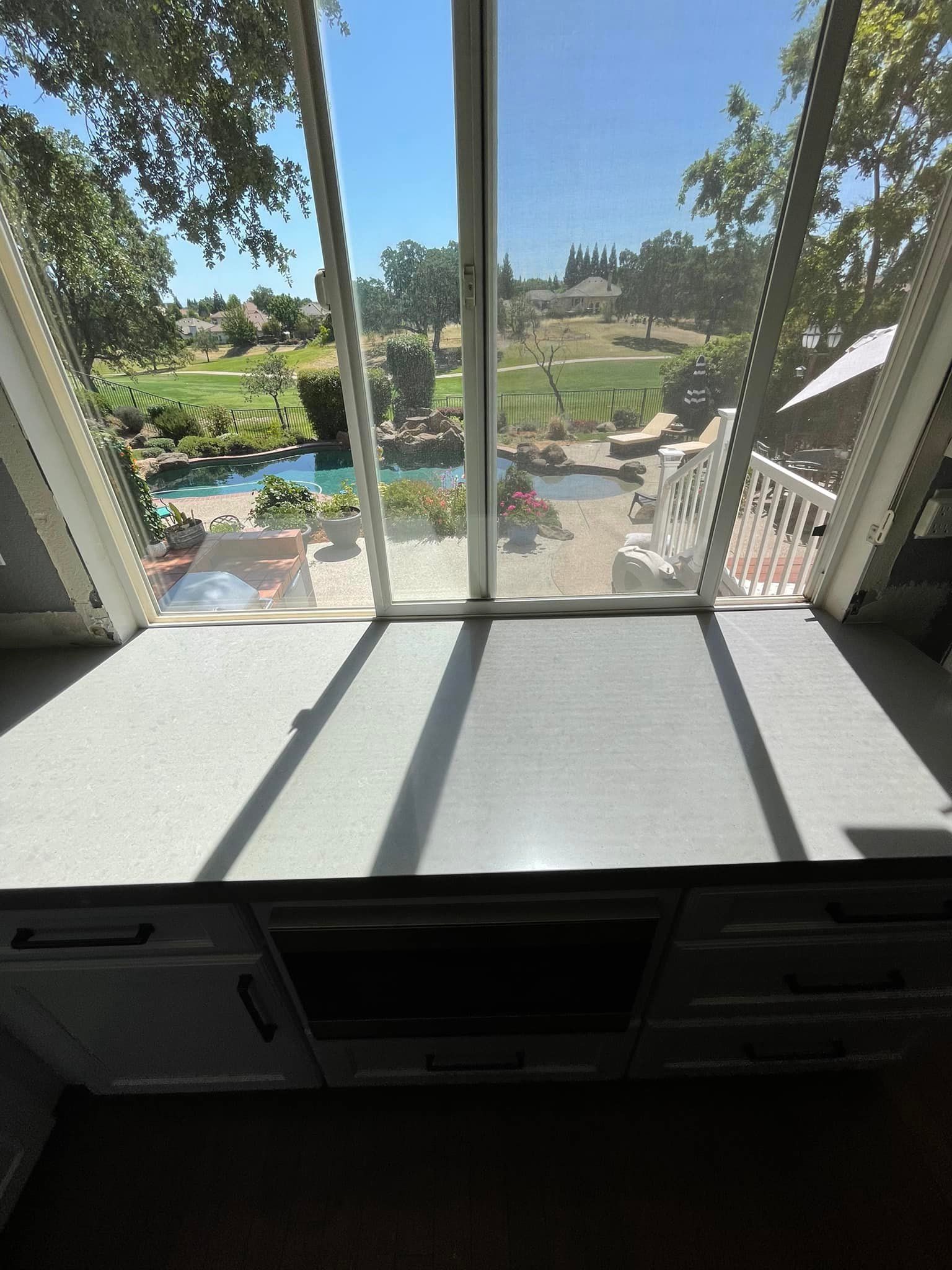A countertop with a view of a backyard with a pool and greenery through a large window.