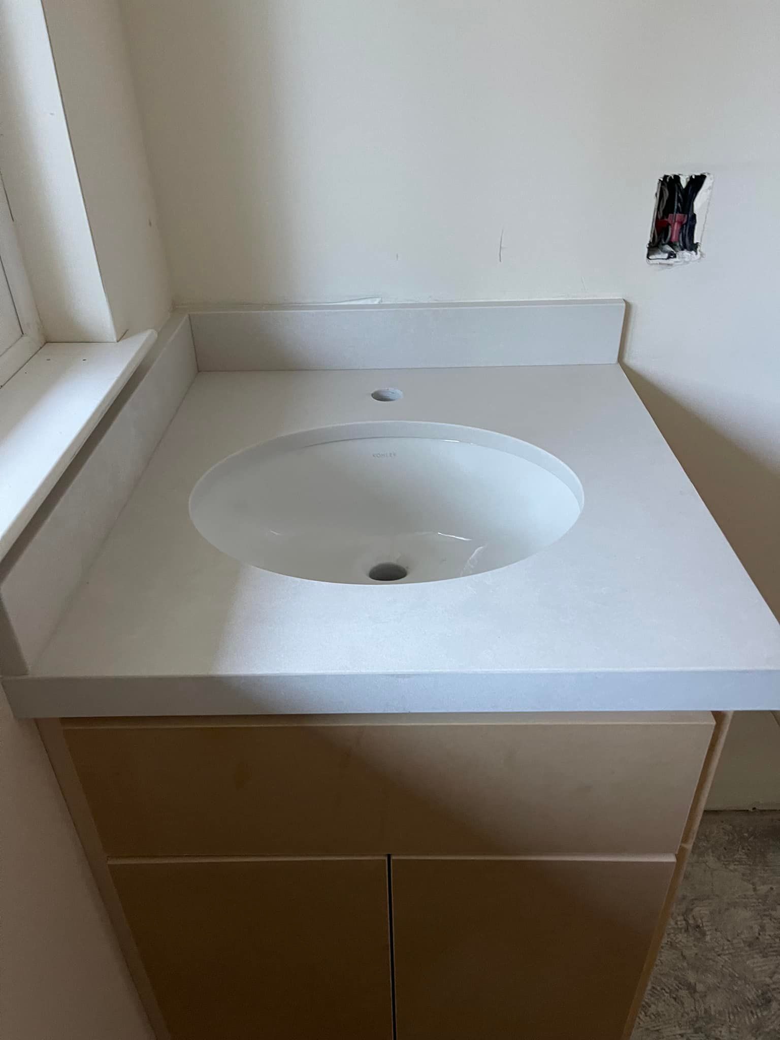 Bathroom vanity with white sink, light countertop, and wood cabinet against a white wall.