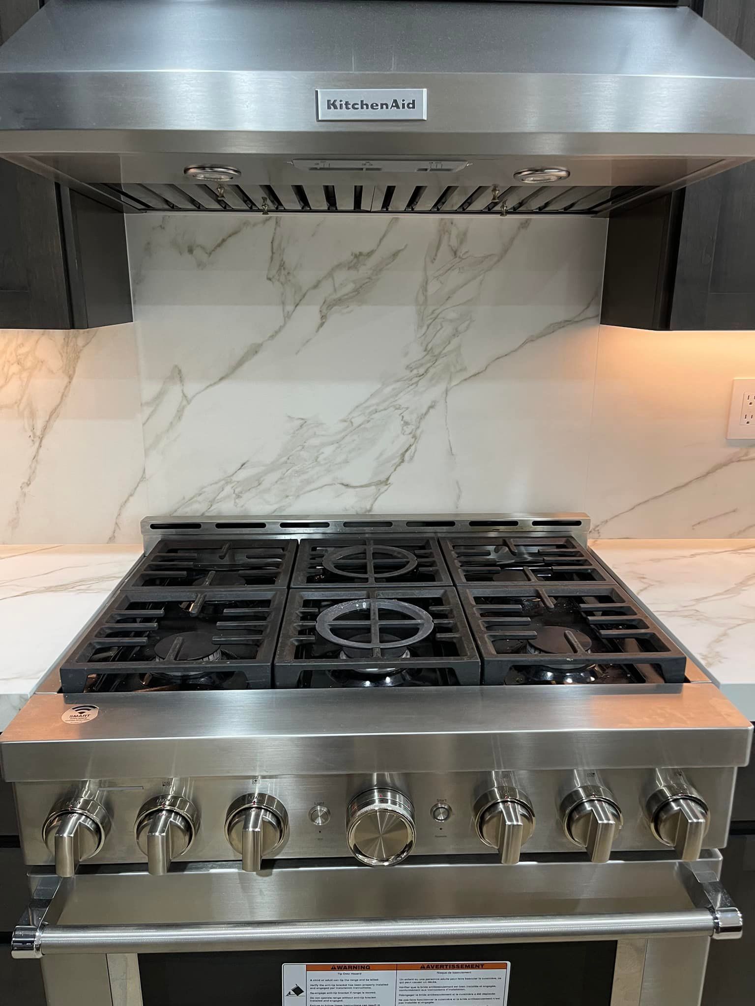 Stainless steel KitchenAid gas range and hood, marble backsplash, and countertop.