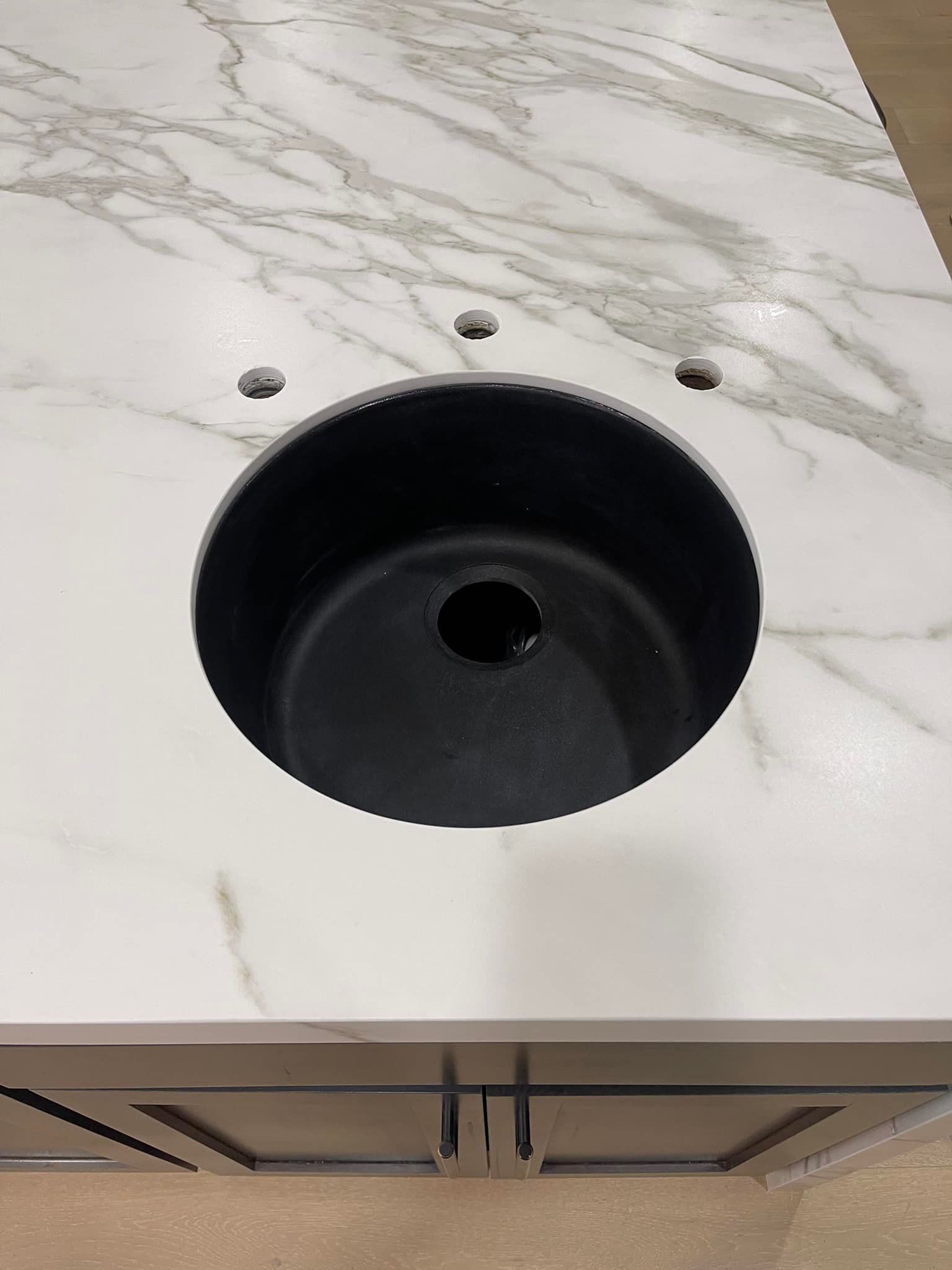 A white marble countertop with a black sink basin and faucet holes. A bathroom vanity is beneath.