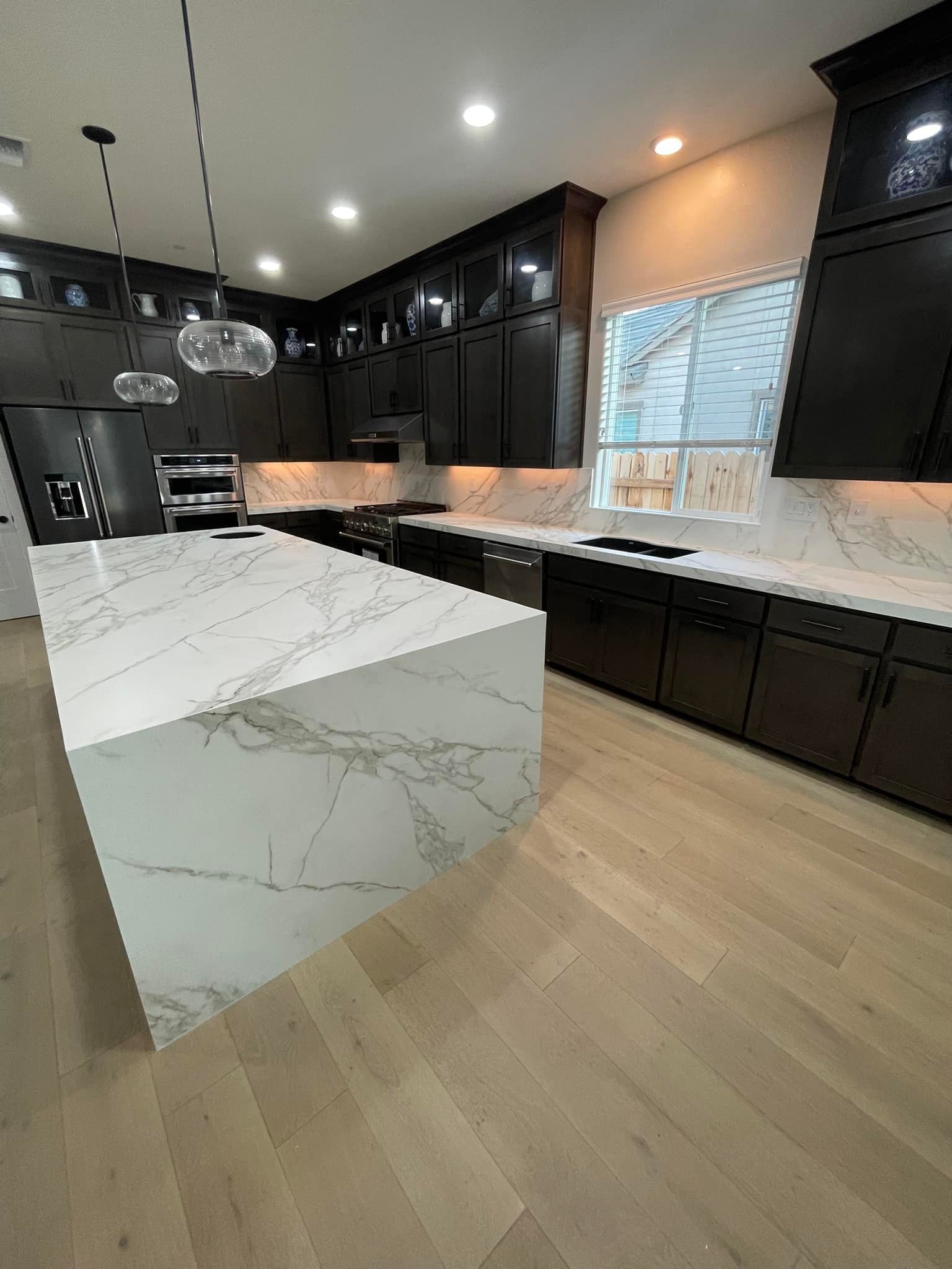 Modern kitchen with white marble island and dark cabinets, light wood floor.