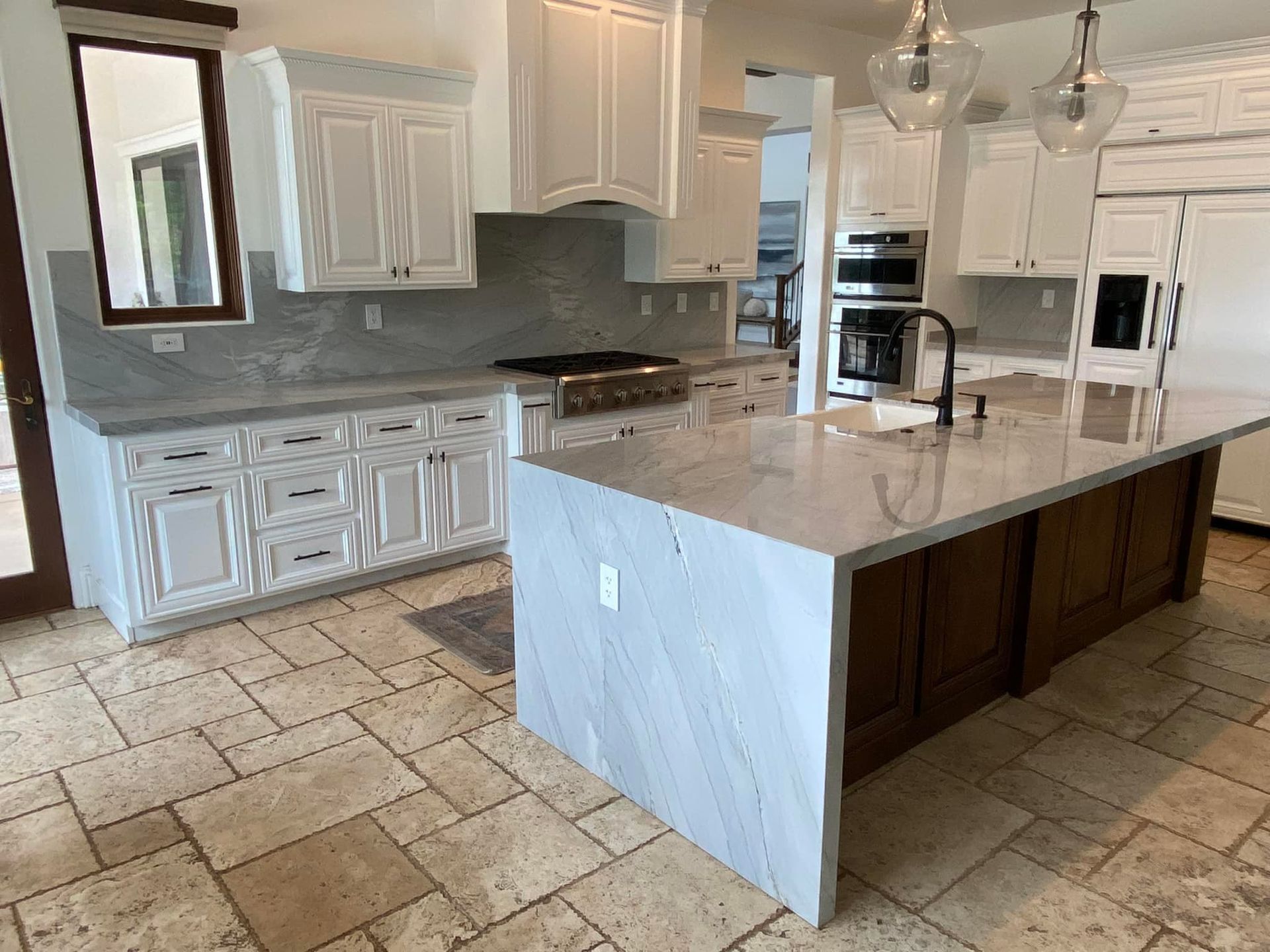 Spacious white kitchen with a large island, granite countertops, and dark wood cabinets.