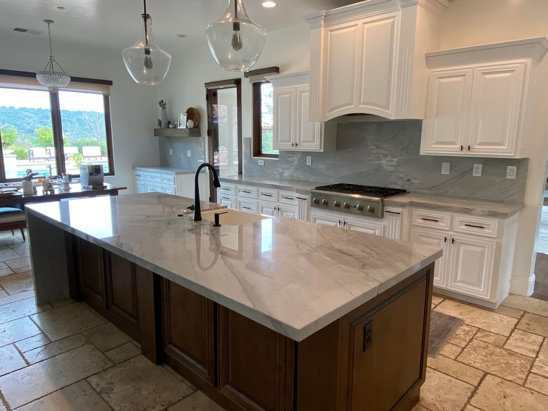 Spacious kitchen with white cabinets, brown island, and stone countertops; overlooking outdoor scenery.