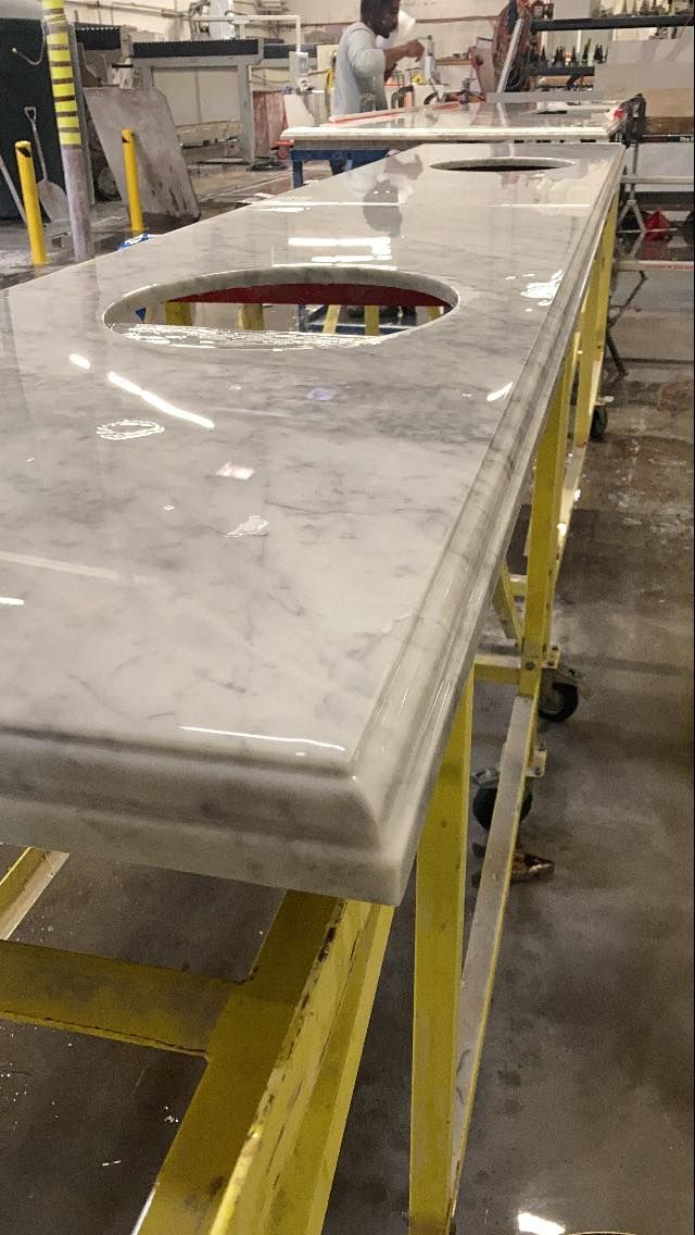 White marble countertop with two sink cutouts, in a workshop with a person working.