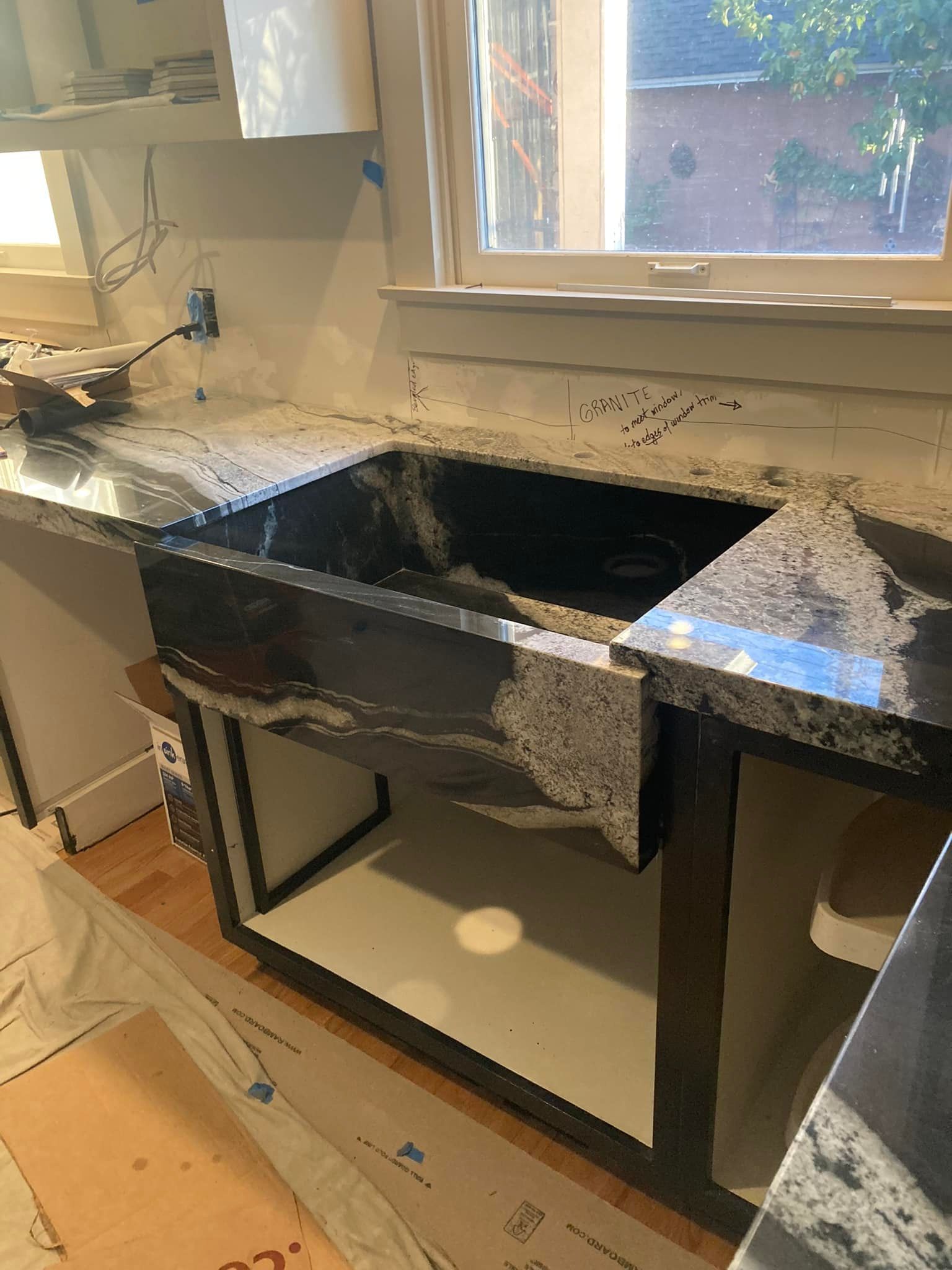 Kitchen sink with dark countertop and open cabinet. Sunlight streams in through window.