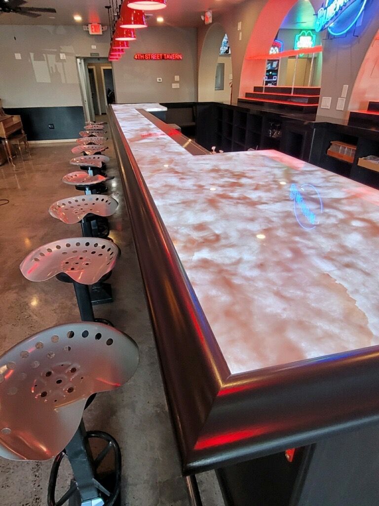 Bar with long, illuminated counter, tractor seat stools, and red lighting.