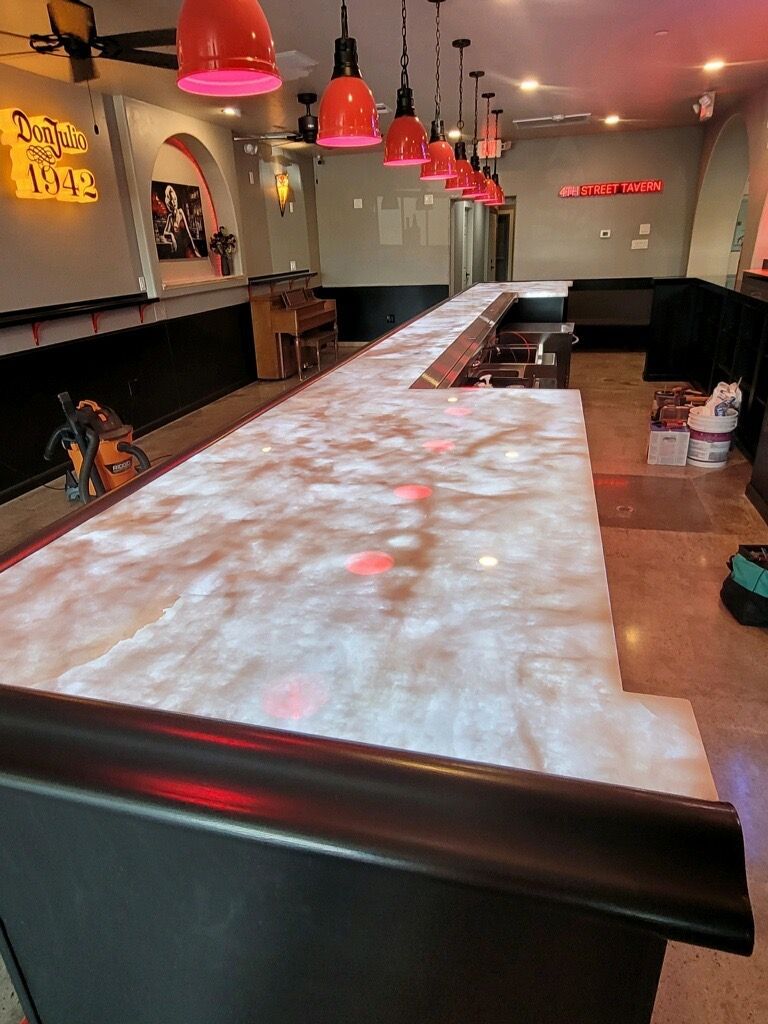 Bar with a long, light-colored countertop, red pendant lights, and dark bar front.